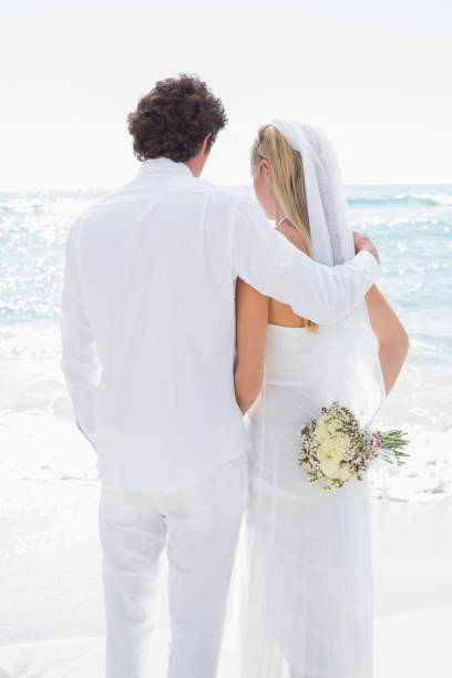 istock Bride and groom looking out to sea embracing 869585062