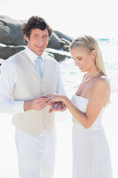 istock Man putting ring on smiling blonde brides finger 869585280