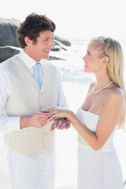 istock Handsome man putting ring on smiling blonde brides finger 869585298