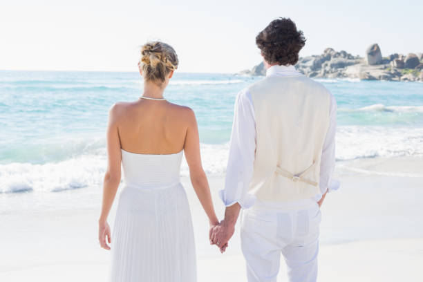 istock Bride and groom holding hands looking out to sea 869587356