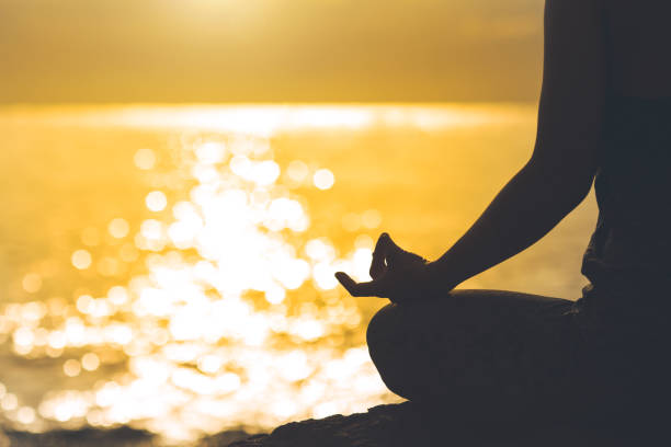 istock Young woman silhouette meditating and practicing yoga on the beach at sunset. 869587402