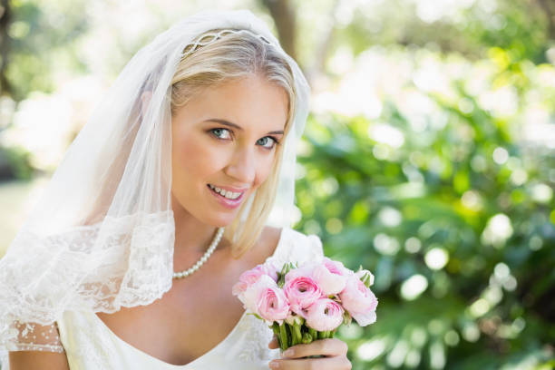 istock Happy bride in a veil holding her bouquet looking at camera 869591678