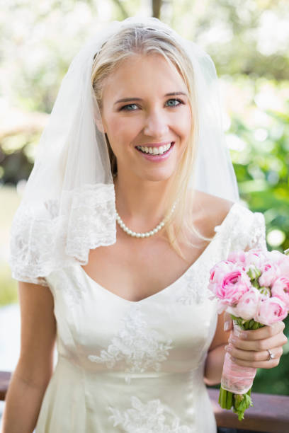 istock Smiling bride in a veil holding her bouquet looking at camera 869591688