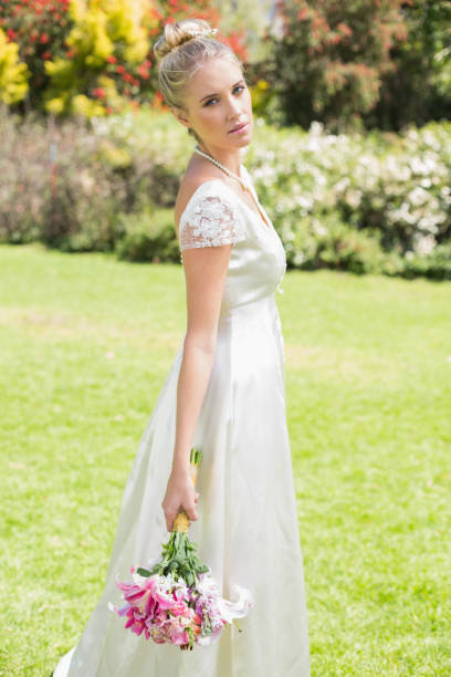 istock Beautiful blonde bride holding bouquet looking at camera 869595270
