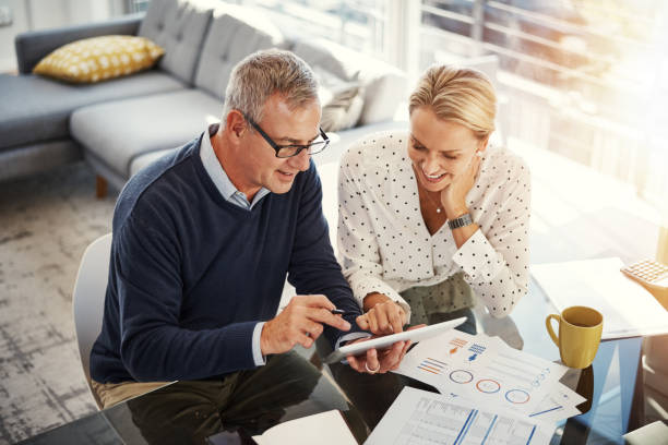 Digitizing the budgeting process Shot of a mature couple using a digital tablet while going through paperwork at home retirement stock pictures, royalty-free photos & images