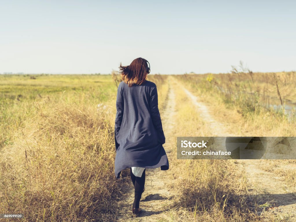 jong meisje dragen van de hoofdtelefoons lopen op vuil weg - Royalty-free Op de rug gezien Stockfoto