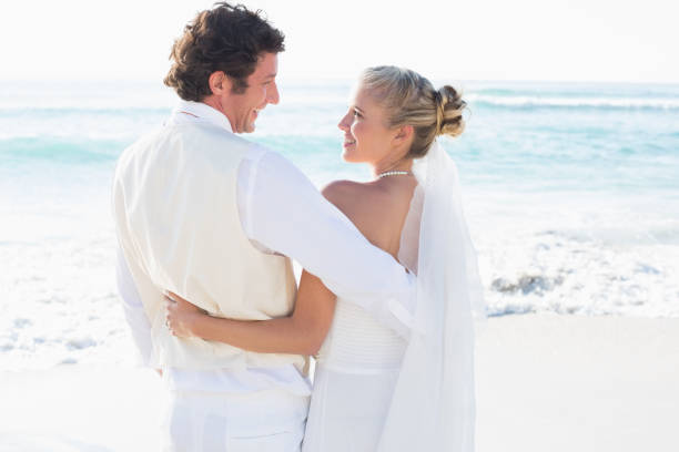 istock Newlyweds standing by the sea smiling at each other 869602786
