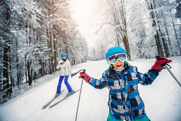 Happy little boy having fun skiing. His mother is following him and filming him with action camera\n