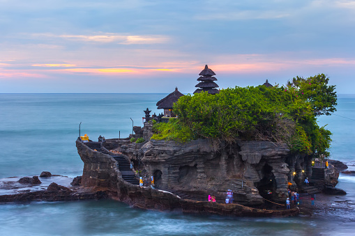 The Pilgrimage Temple of Pura Tanah Lot at sunset, island with an Indonesian shrine on the ocean, long exposure, copy space for text.