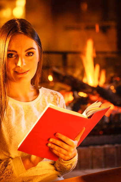 istock Woman reading book at fireplace. Winter home relax 869629354