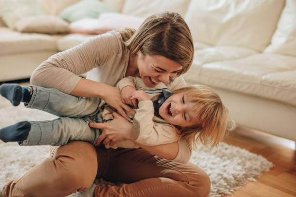 madre gioiosa e suo figlio piccolo che si divertono a casa. - tickling foto e immagini stock