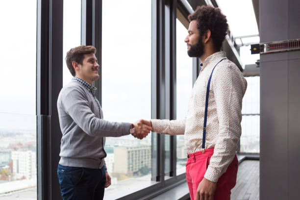 istock Two young businessmen shaking hands in modern office hall. 869634944
