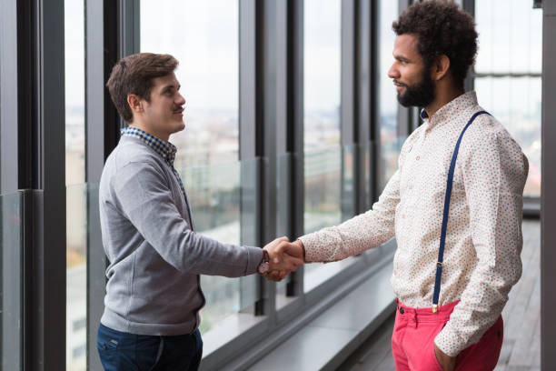 istock Two young businessmen shaking hands in modern office hall. 869635012