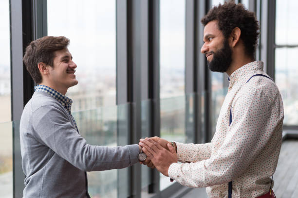 istock Two young businessmen shaking hands in modern office hall. 869635466