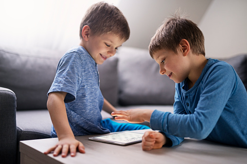 Two little boys are playing chess using modern tablet with chess application. Brothers are having fun during the game.


