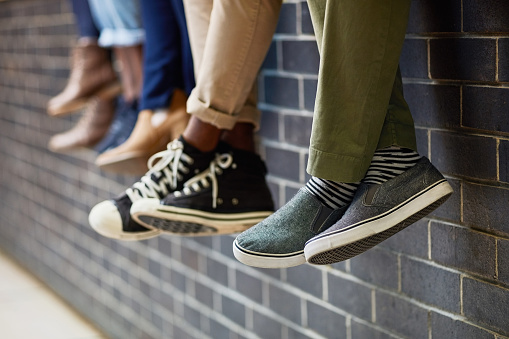 Closeup shot of an unidentifiable group of university students sitting together on a wall outside