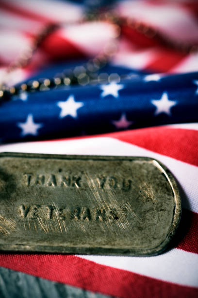 text thank you veterans in a dog tag closeup of a rusty dog tag with the text thank you veterans engraved in it, next to a flag of the United States, on a rustic wooden surface thank you veterans day stock pictures, royalty-free photos & images