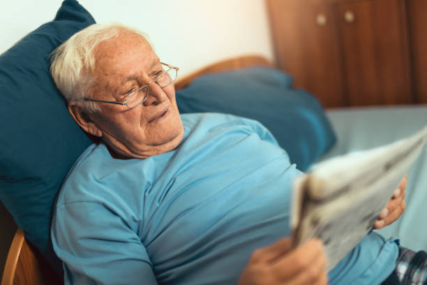 istock Senior man in glasses reading newspaper at home 869642464