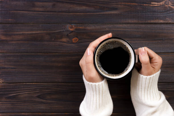 solitaria mujer tomando café en la mañana, la vista superior de mujer manos sostener taza de bebida caliente en el mostrador de madera - café bebida fotografías e imágenes de stock