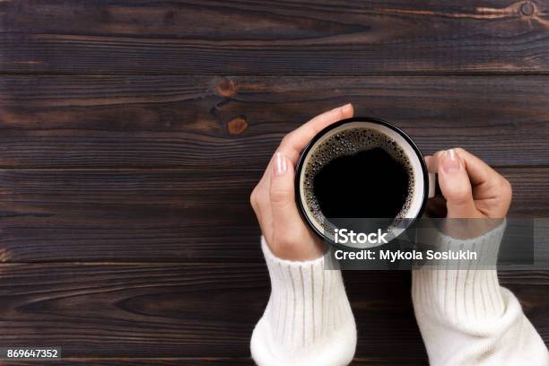 Lonely Woman Drinking Coffee In The Morning Top View Of Female Hands Holding Cup Of Hot Beverage On Wooden Desk Stock Photo - Download Image Now