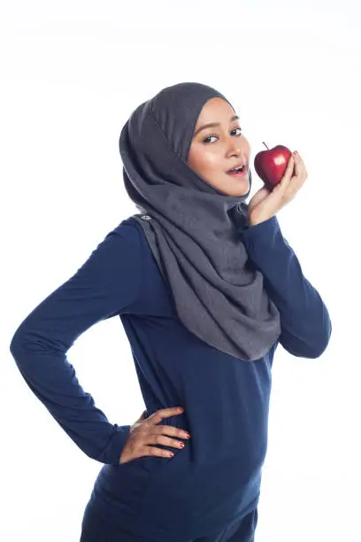 A young beautiful hijab sportsgirl is holding an apple looking at camera isolated with white background