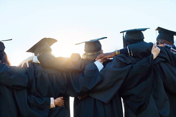 This is just the beginning Rearview shot of a group of students standing in a row on graduation day cap hat photos stock pictures, royalty-free photos & images
