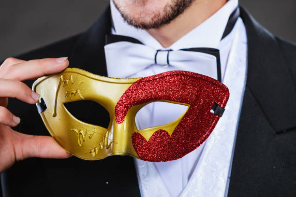 Holidays, people and celebration concept. Male hand holding red golden carnival mask closeup on dark