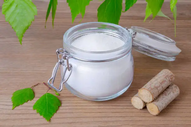 Photo of sugar substitute xylitol, a glass jar with birch sugar, liefs and wood