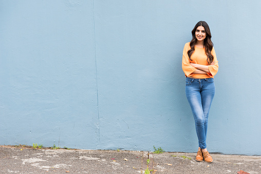 Portrait photo of young woman standing against a wall in casual clothing