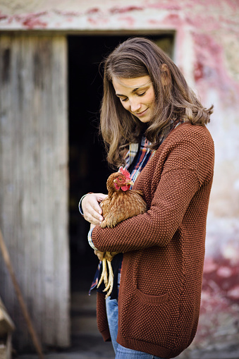 Caucásica joven mujer con cabello rubio tiene una gallina en una granja photo