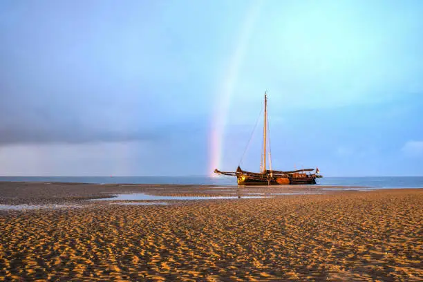 Clipper drying of on the tidal mudflats of the Wadden Sea, North Sea, Europe. Rainbow in the background.