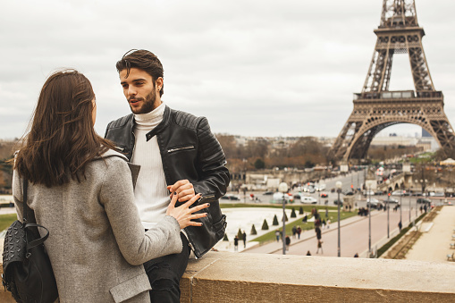 Young tourists enjoying the romantic day in Pairs. They are at the surrounding wall with a beautiful view on Eiffel tower and crowded square.
