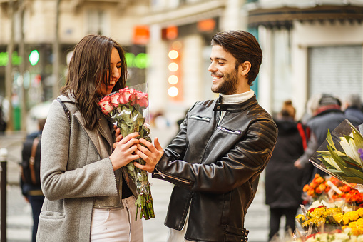 Young man is on a street market with his girlfriend, and buys her a lovely bouquet of roses. She is excited.