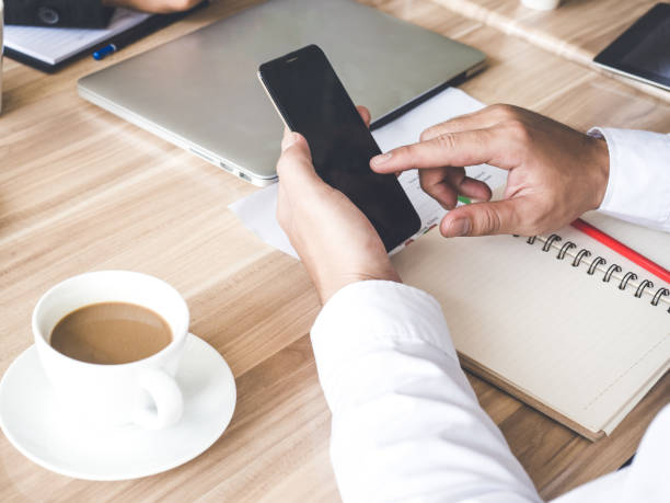 istock Meeting table/desk, businessman using smart phone and checking business plan, progress report for business work, financial report, status, tablet, coffee, on table, discussing with colleague at office 869694806