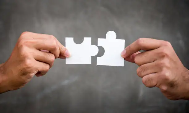 Two hands of businessman holding jigsaw/puzzle for teamwork cooperation and togetherness concept
