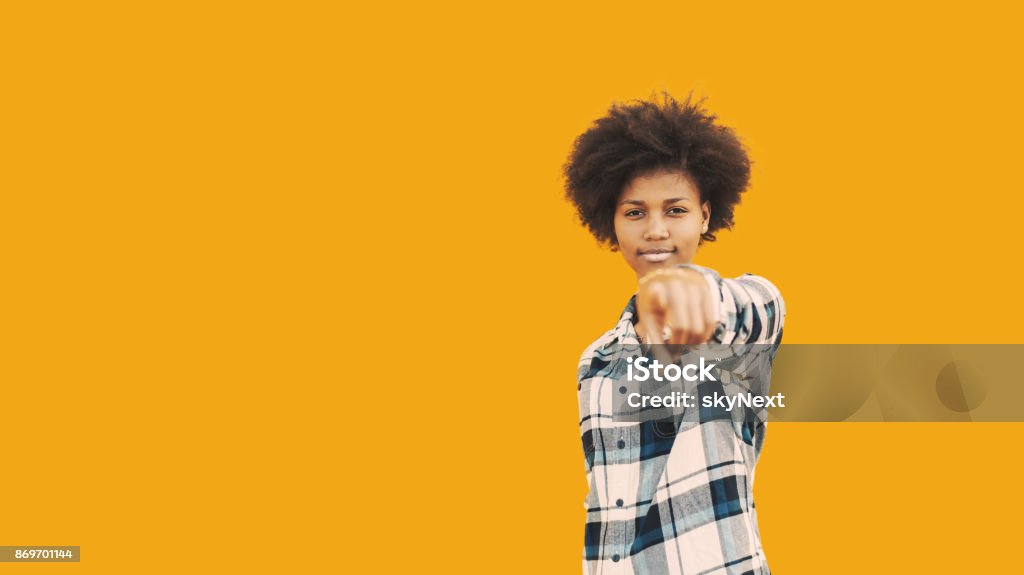 African american hipster girl on yellow background Portrait of beautiful self-confident black student girl standing in front of isolated yellow solid background and pointing with her finger on camera; with copy space zone for advertising text or logo Adult Stock Photo