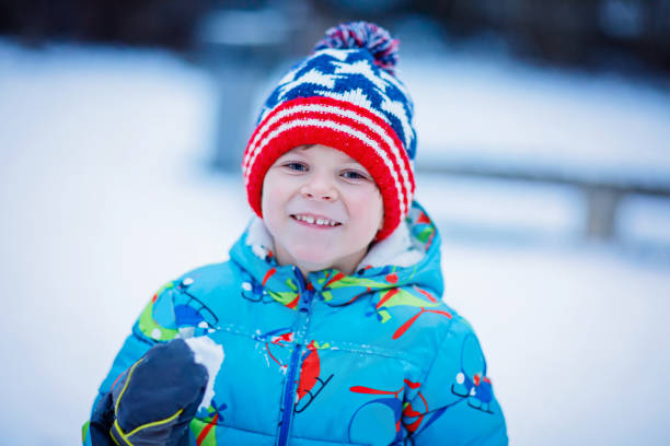 Funny little kid boy in colorful clothes playing outdoors during snowfall. Active leisure with children in winter on cold snowy days. Happy child on winter vacations in Switzerland
