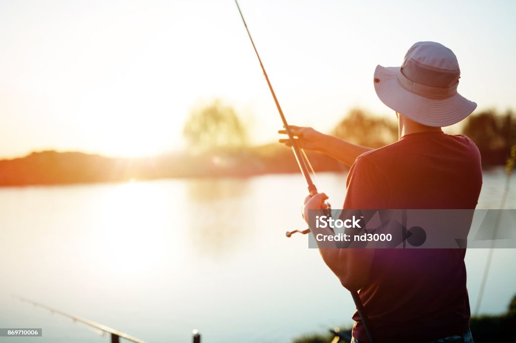 Young man fishing on a lake at sunset and enjoying hobby Young man fishing on a lake at sunset and enjoying hobby and recreation Fishing Stock Photo