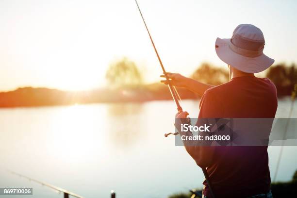 Young Man Fishing On A Lake At Sunset And Enjoying Hobby Stock Photo - Download Image Now