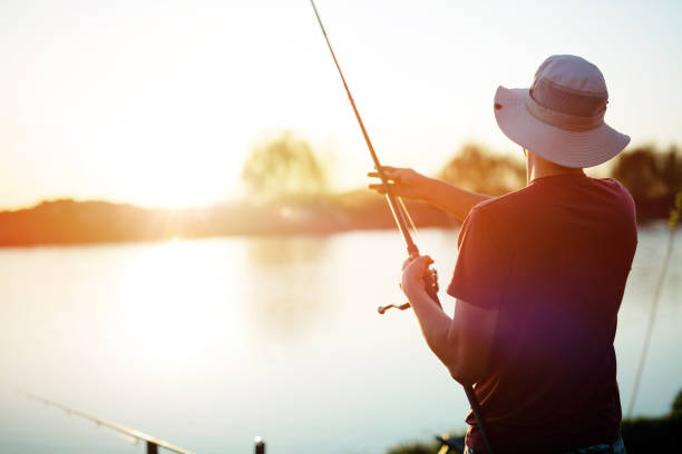 young man fishing on a lake at sunset and enjoying hobby - fishing supplies imagens e fotografias de stock