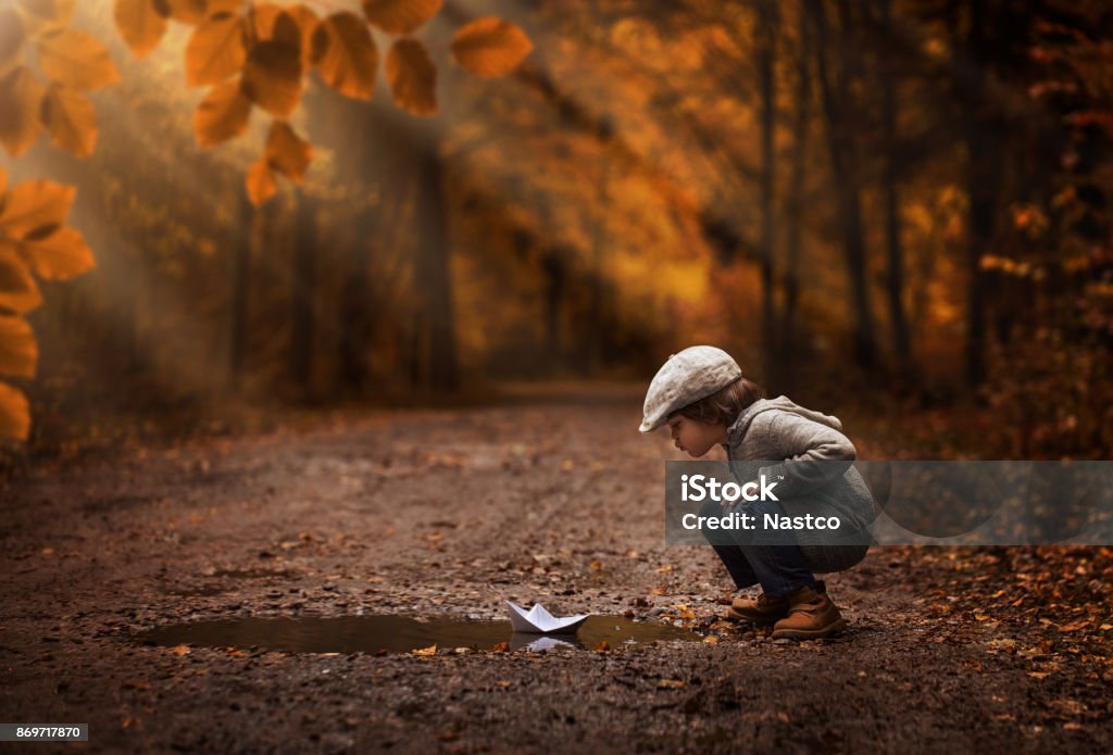 Cute boy playing with paper boat Little boy playing with the paper boat in the autumn forest puddle Child Stock Photo