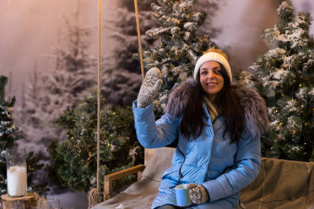 istock Female in blue down jacket greeting while sitting on a swing in a snow-covered park 869723182