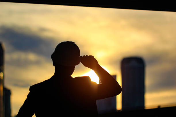 istock Silhouette of engineer standing survey work on construction site and hold security helmet on sunset background 869723540