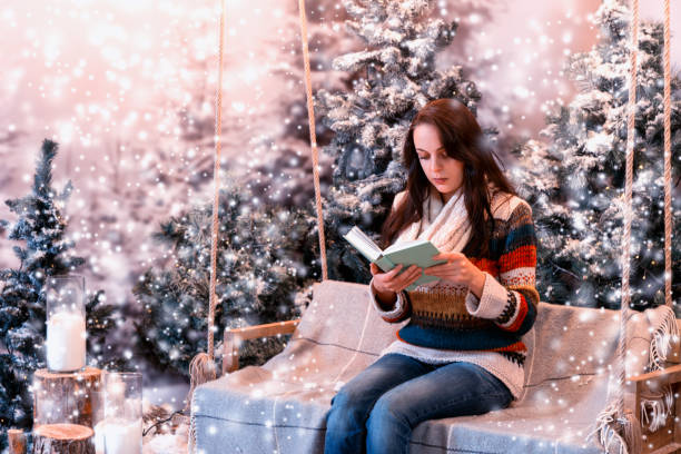 istock Young woman reading a book while sitting on a swing with a blanket in a snow-covered park 869723554