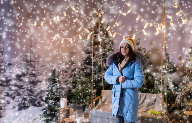 istock Female in blue down jacket standing near bench or a swing with a blanket under the flashlights in a snow-covered park 869725934