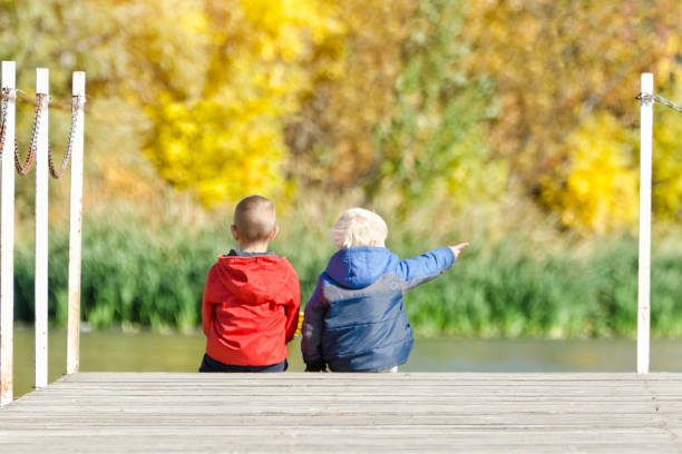 istock Two boys are sitting on the pier. Autumn. Back view. 869726000