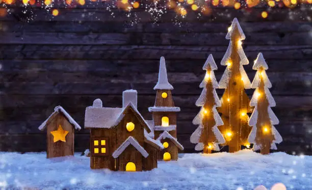 Christmas background with illuminated wooden village and trees. Dark wooden background with free space for text. Celebration of christmas