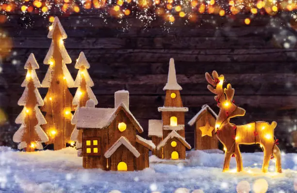 Christmas background with illuminated wooden village, moose and trees. Dark wooden background with free space for text. Celebration of christmas