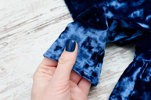 Sleeve of blue velvet dress in female hand. Fashionable concept.