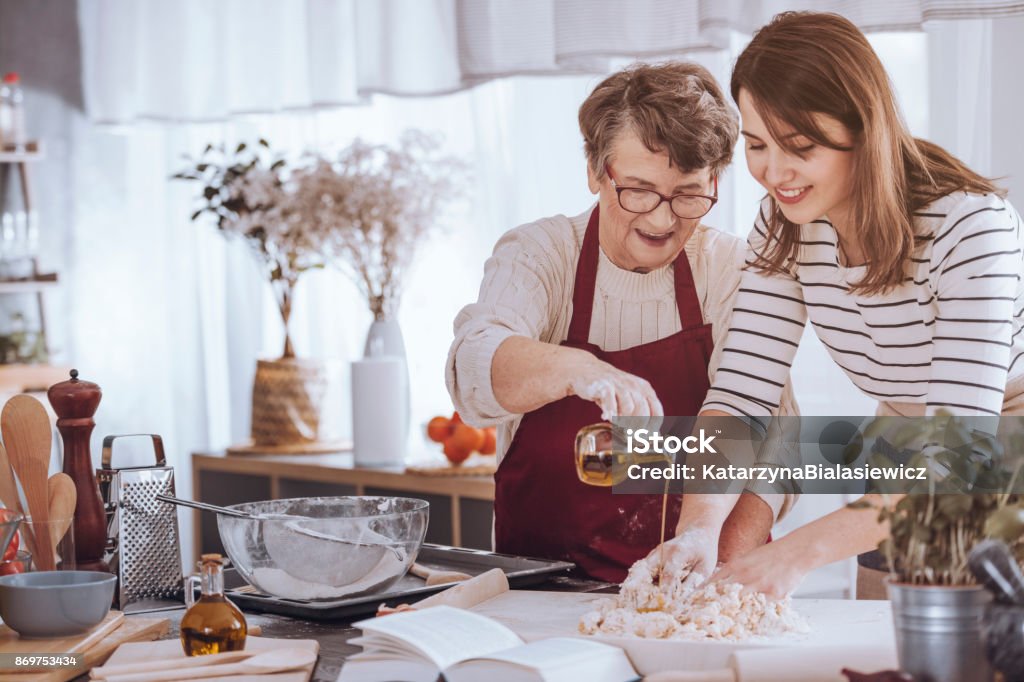 Grandmother adding oil to dough Grandmother helping her granddaughter make dough by adding olive oil Christmas Stock Photo